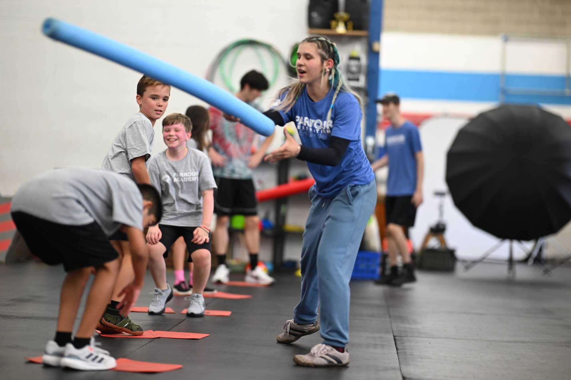 Coach swinging a pool noodle while students duck and laugh