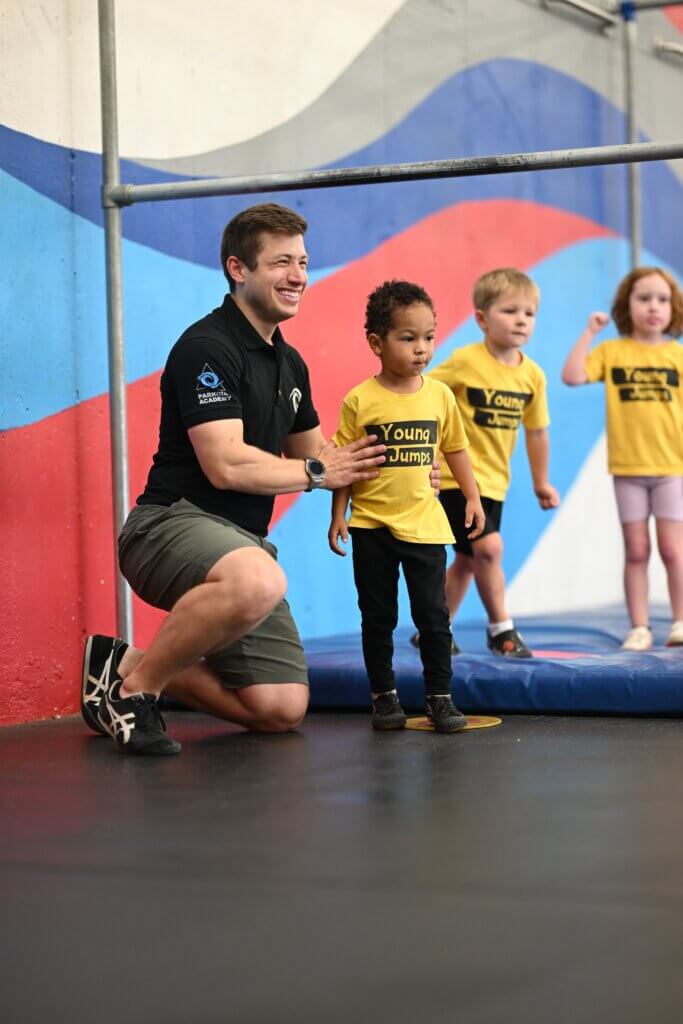 Young Jumps - coach and child Parkour coach kneeling beside a smiling preschooler in a Young Jumps T-shirt